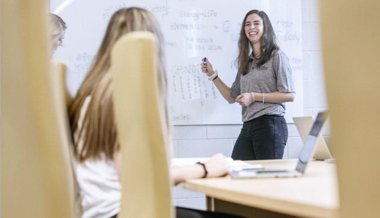 woman smiling and pointing to whiteboard