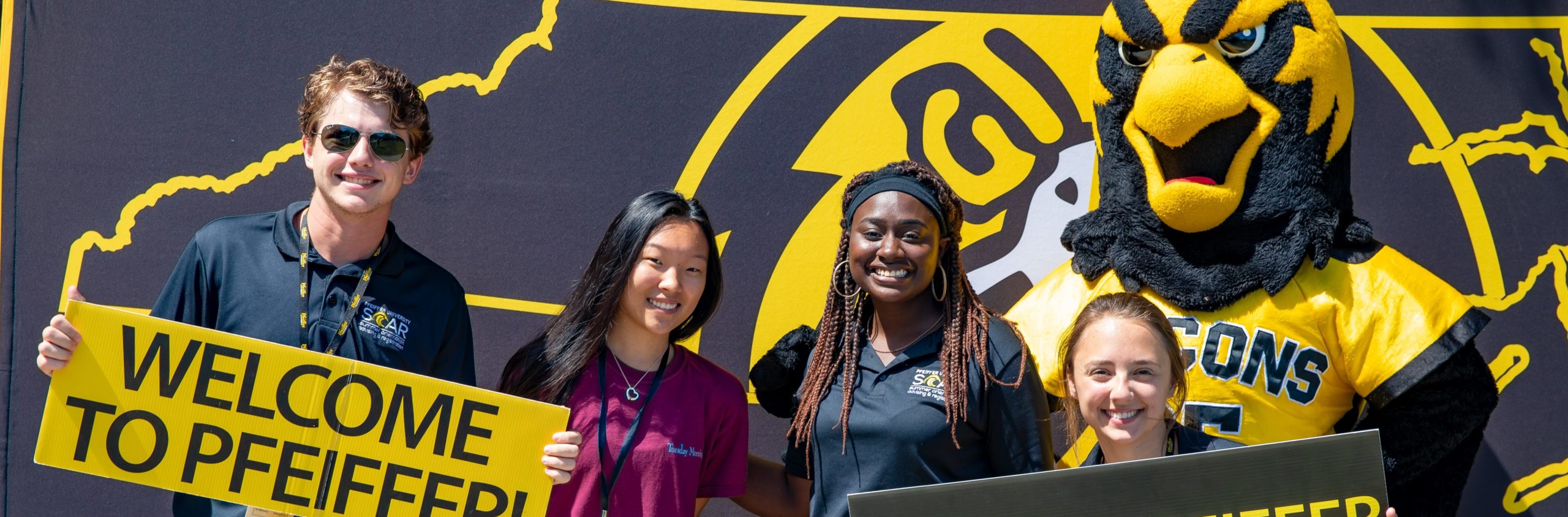 Group of students with Pfeiffer mascot and welcome sign