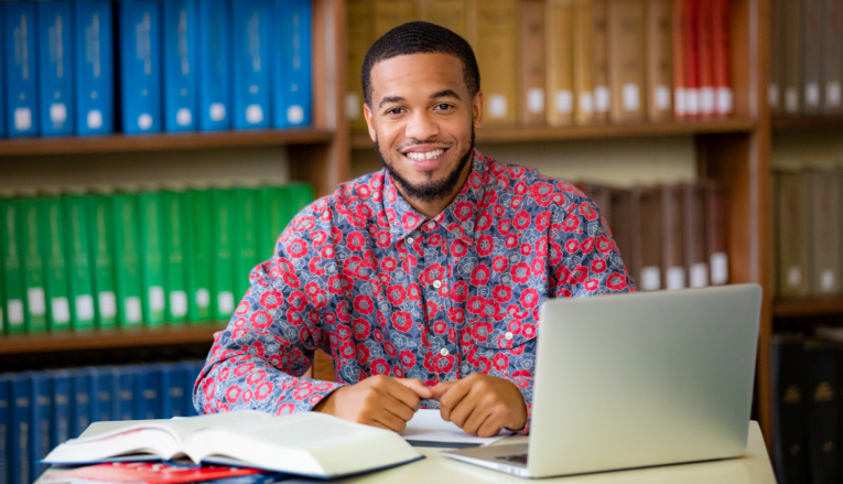 man smiling at desk with laptop and book