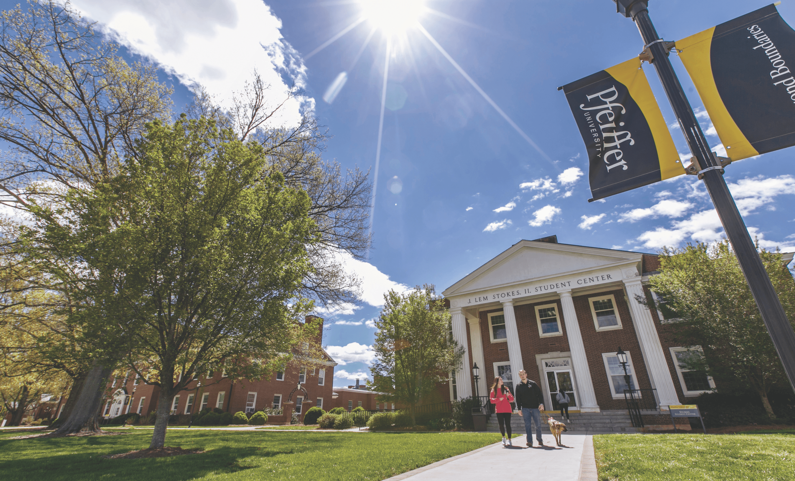 blue sky shining on pfeiffer building with students walking dog