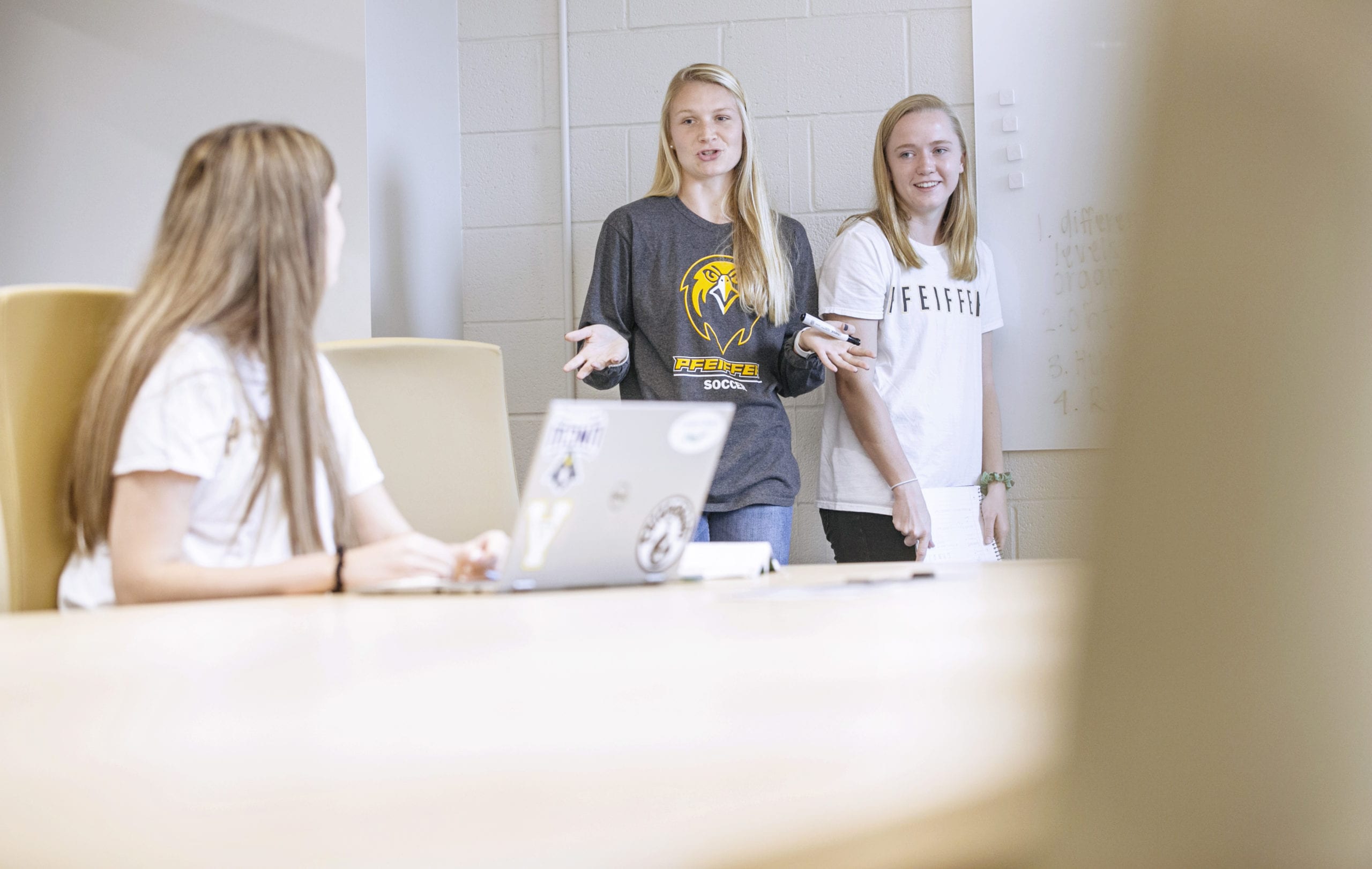 2 girls talking to another girl in a classroom