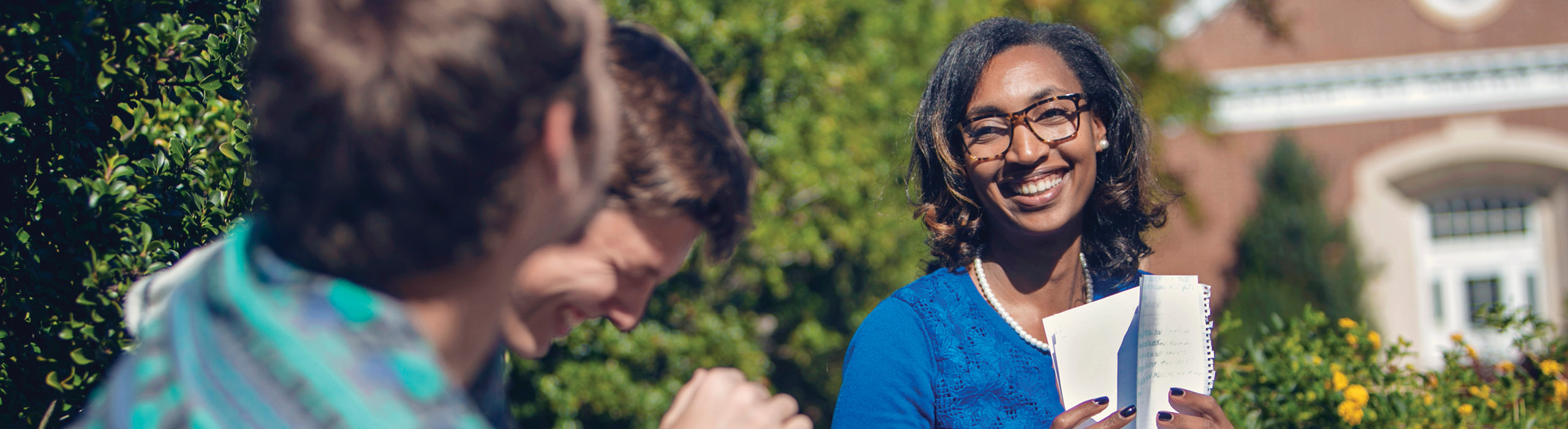 Three students sitting outside talking and smiling