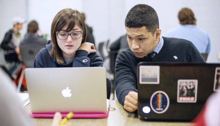 two students working on laptops in class