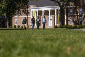 Group of students walking across campus lawn