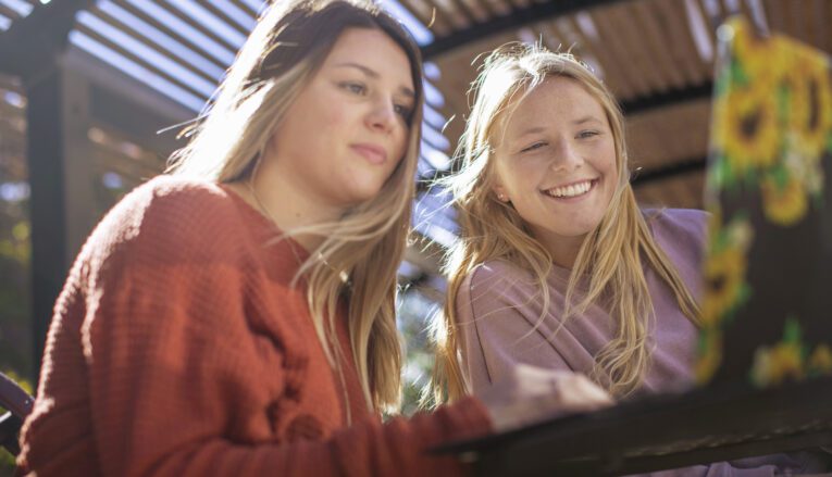 Two young women smiling while looking at a laptop